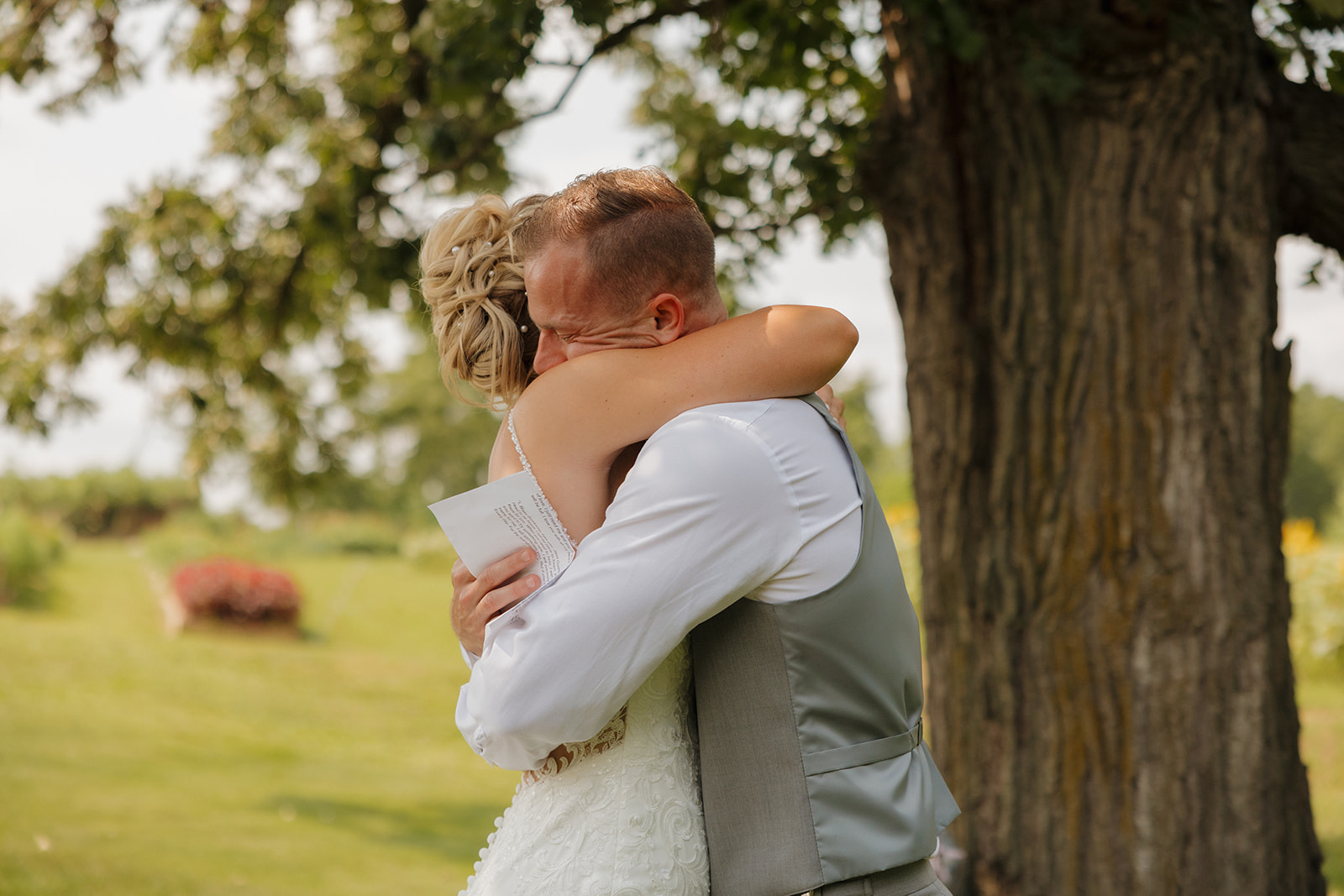 Couple sharing a tight, emotional hug under a tree after reading their vows—pure connection.