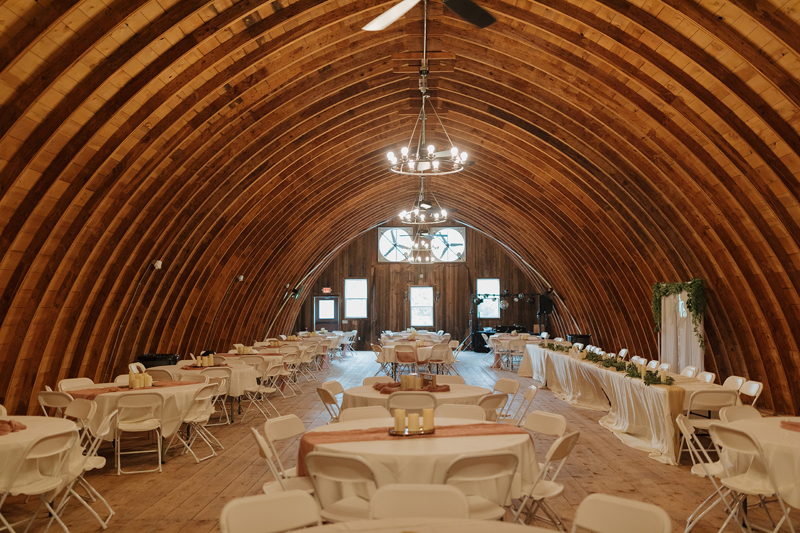 Wide shot of the reception barn, with round tables and soft rustic decor.