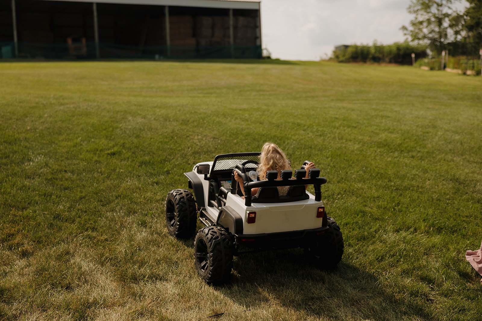 Toddler driving a toy Jeep up the grassy hill as part of a playful wedding ceremony entrance.