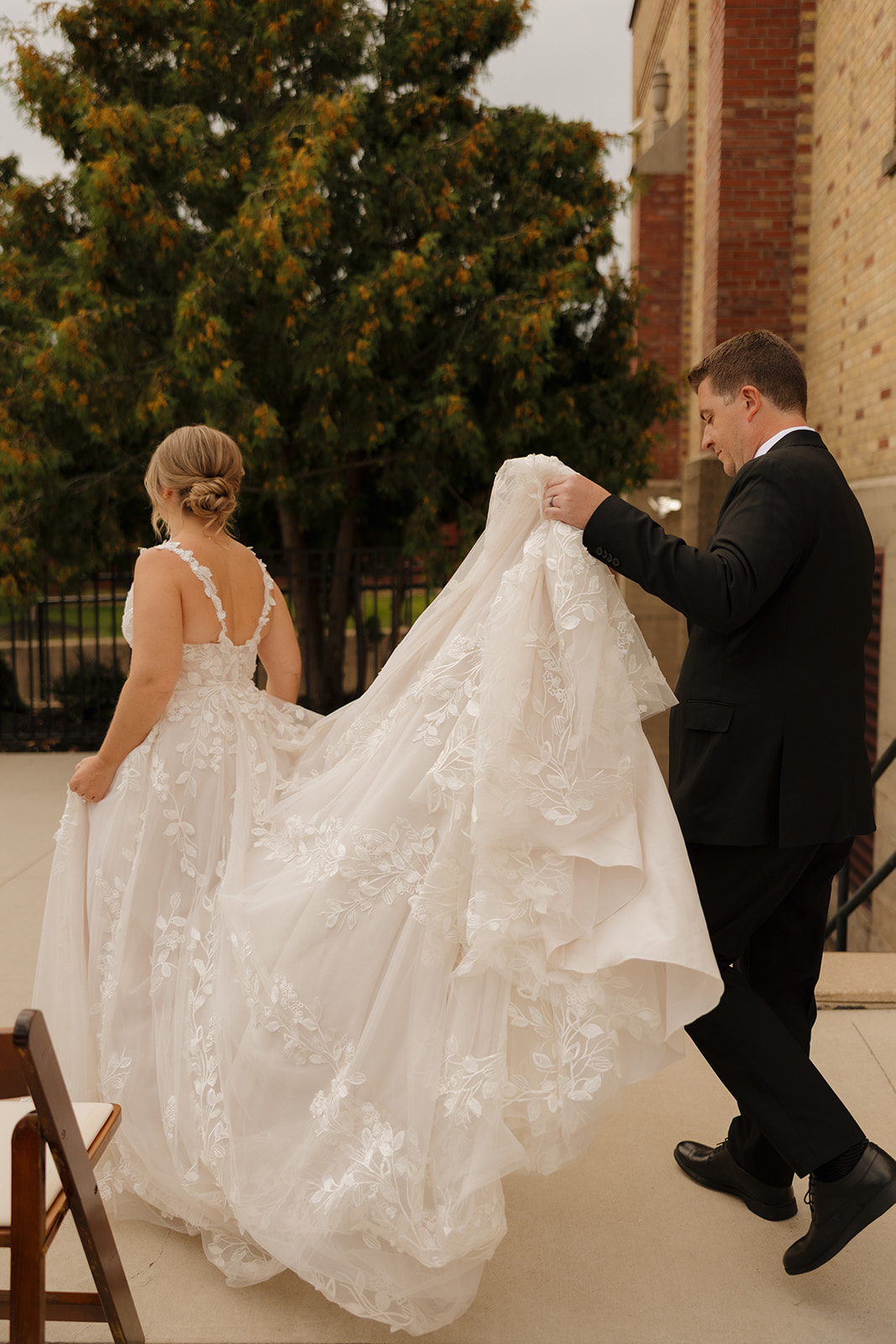 Groom helping carry the bride’s dress as they walk together outside a charming wedding venue in Fort Myers