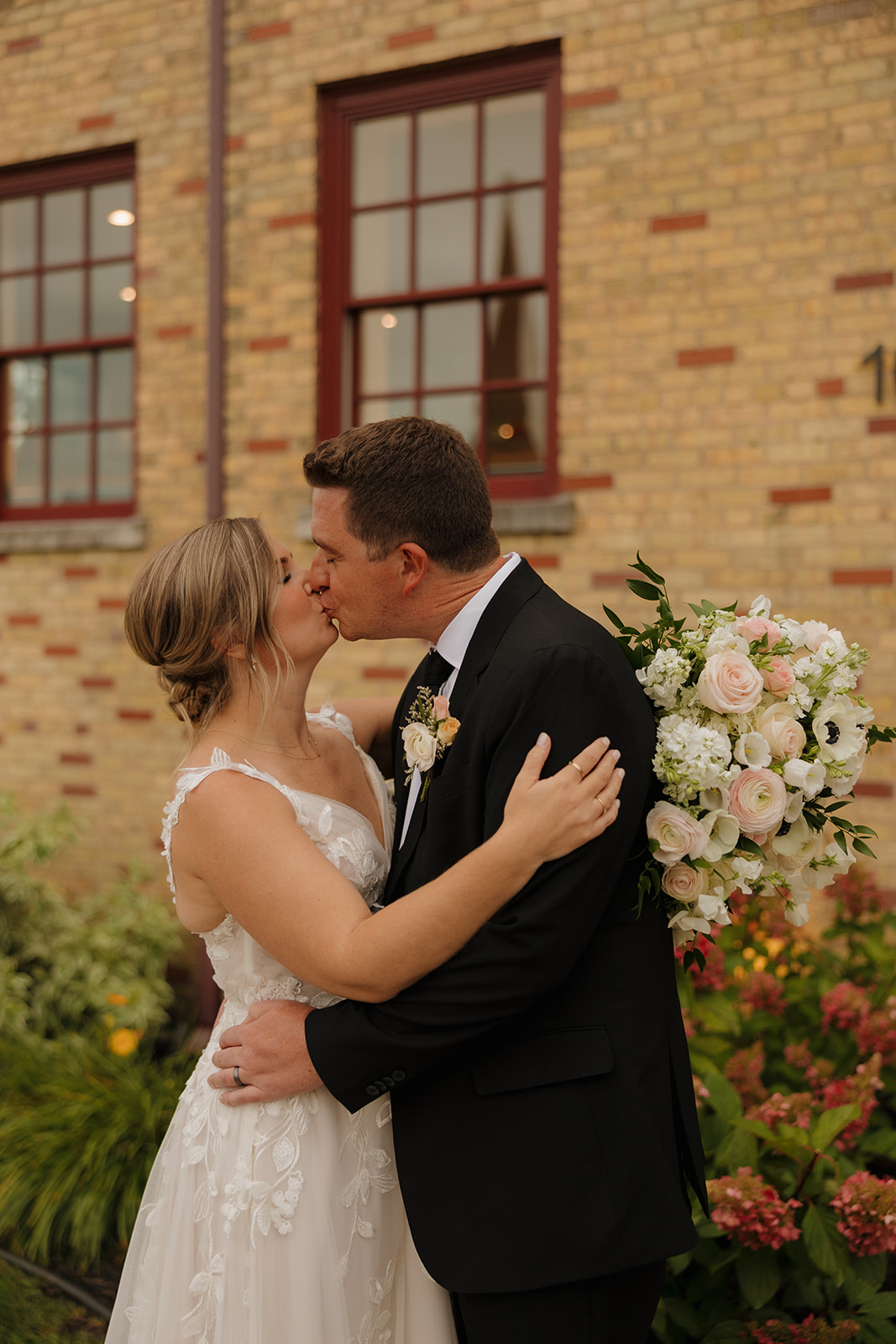 Bride and groom sharing a kiss in front of a historic brick building during romantic wedding portraits.