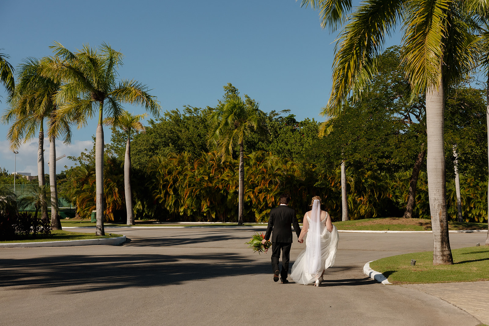 Bride and groom walking hand in hand down a palm-lined road after their ceremony at a beautiful wedding venue in Fort Myers.