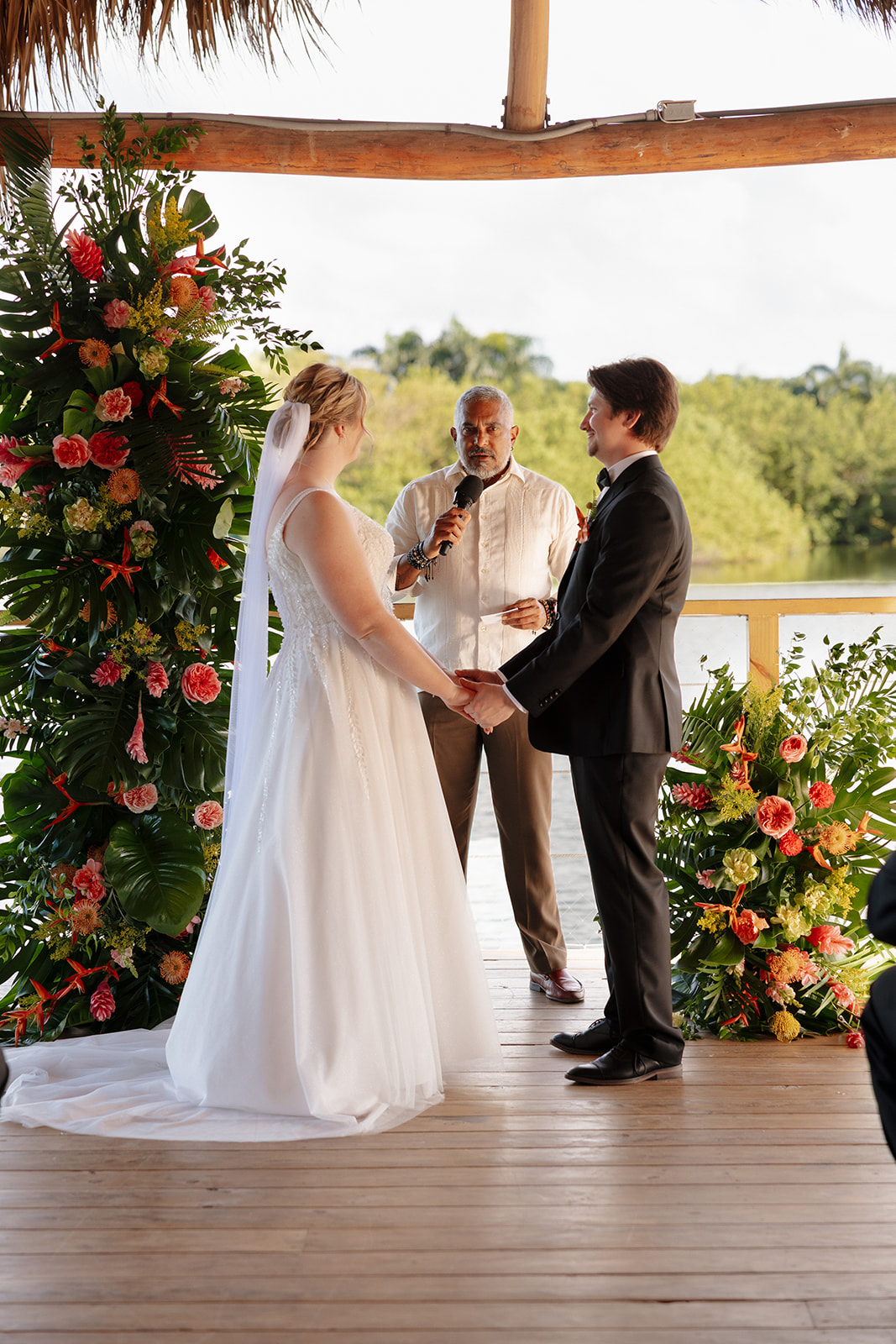 Couple holding hands during their waterfront ceremony surrounded by tropical flowers at one of the most scenic wedding venues in Fort Myers.