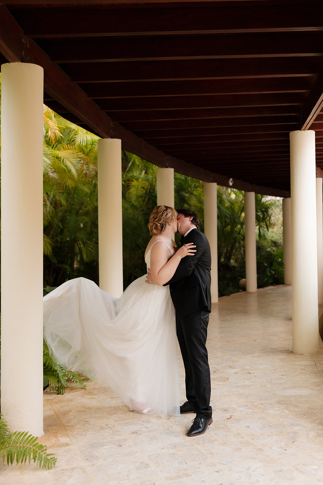Bride and groom embracing under a covered walkway surrounded by tropical greenery at a wedding venue in Fort Myers.