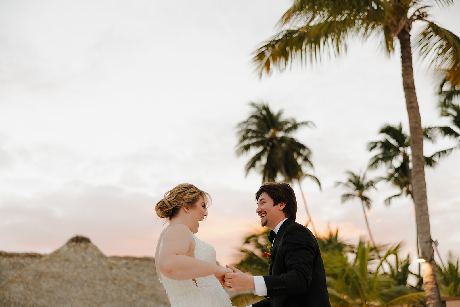 Bride and groom laughing together under palm trees at sunset at one of the most romantic wedding venues in Fort Myers.