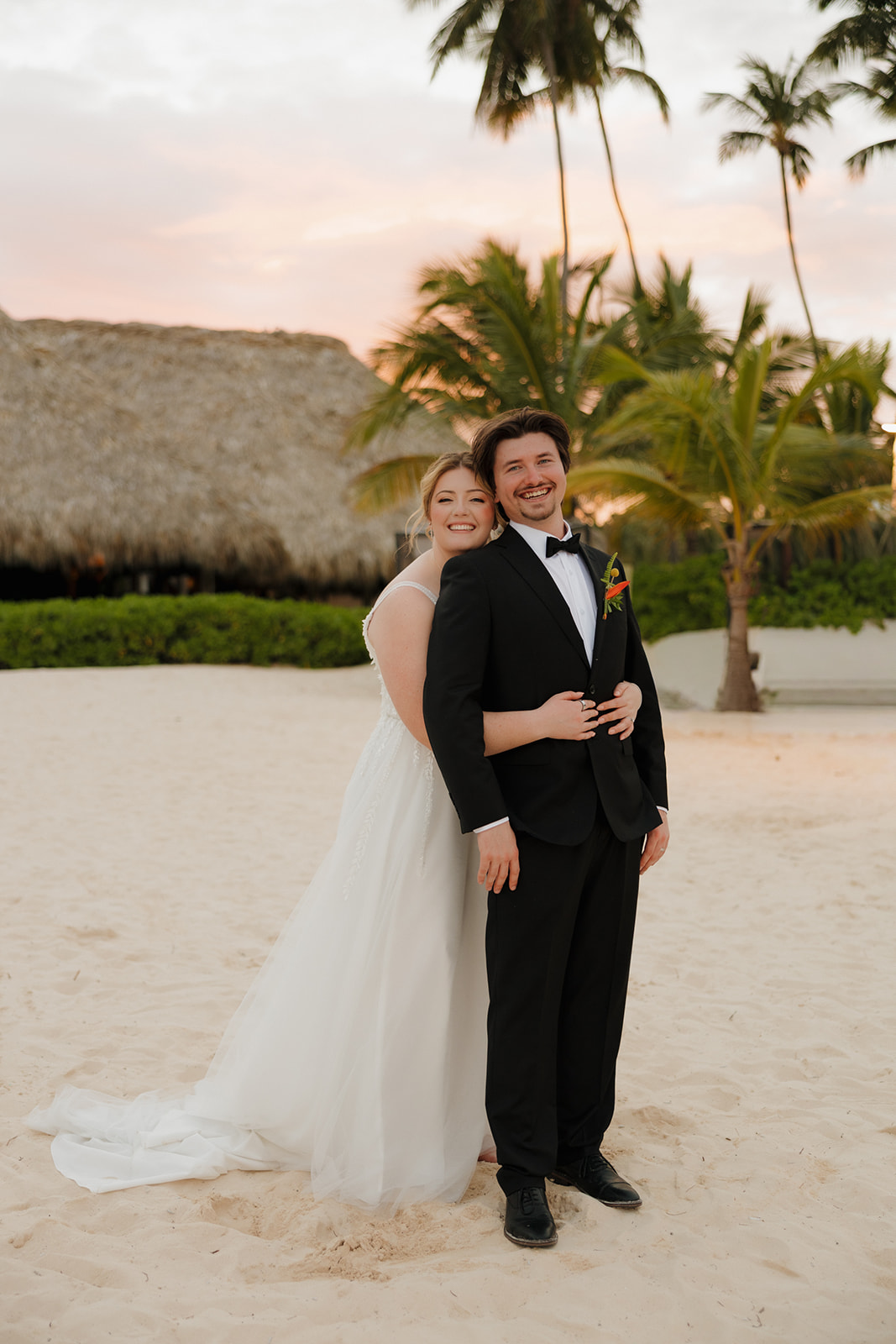 Newlyweds smiling together on a sandy beach with palm trees and sunset sky at a tropical wedding venue in Fort Myers.