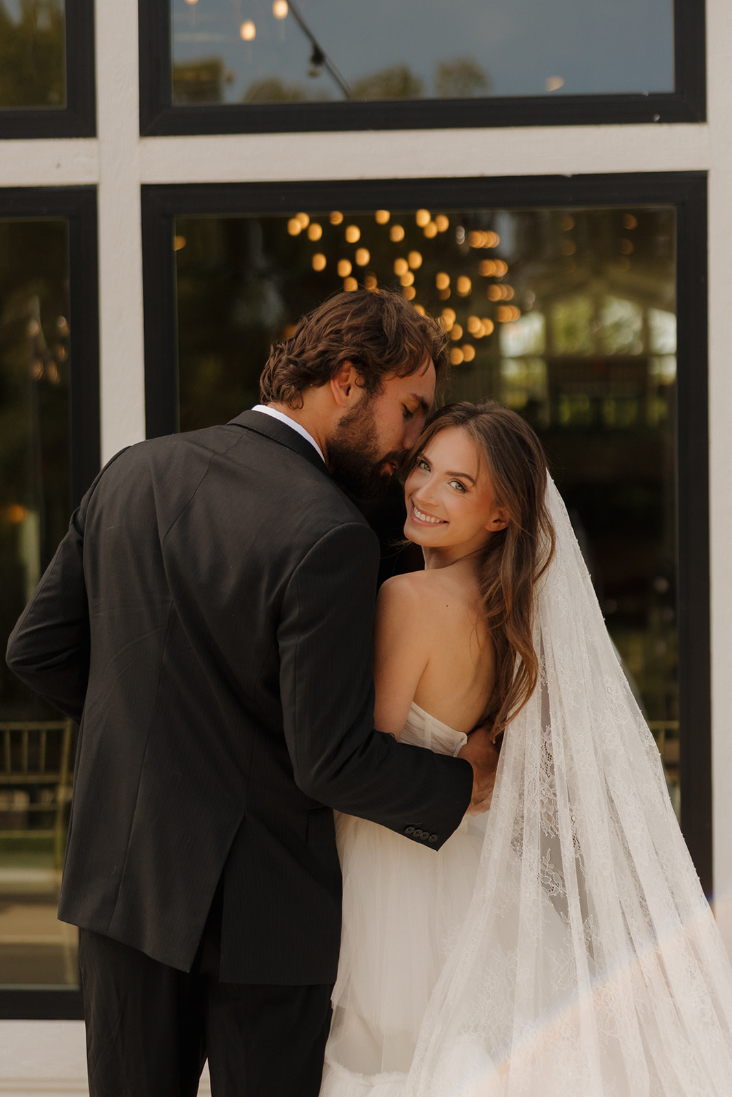 Bride and groom embracing during romantic sunset portraits outside a modern wedding venue