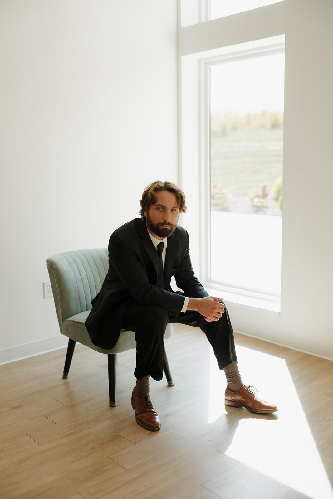 Groom sitting by a window in a minimalist wedding suite getting ready before the ceremony.