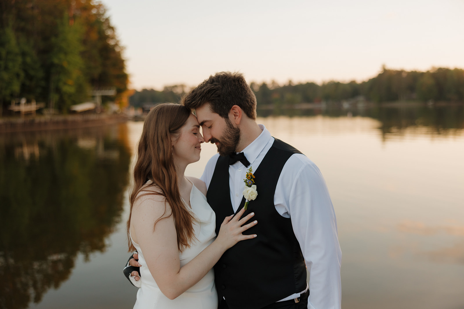 Romantic lakeside wedding portrait of bride and groom holding each other during golden hour.