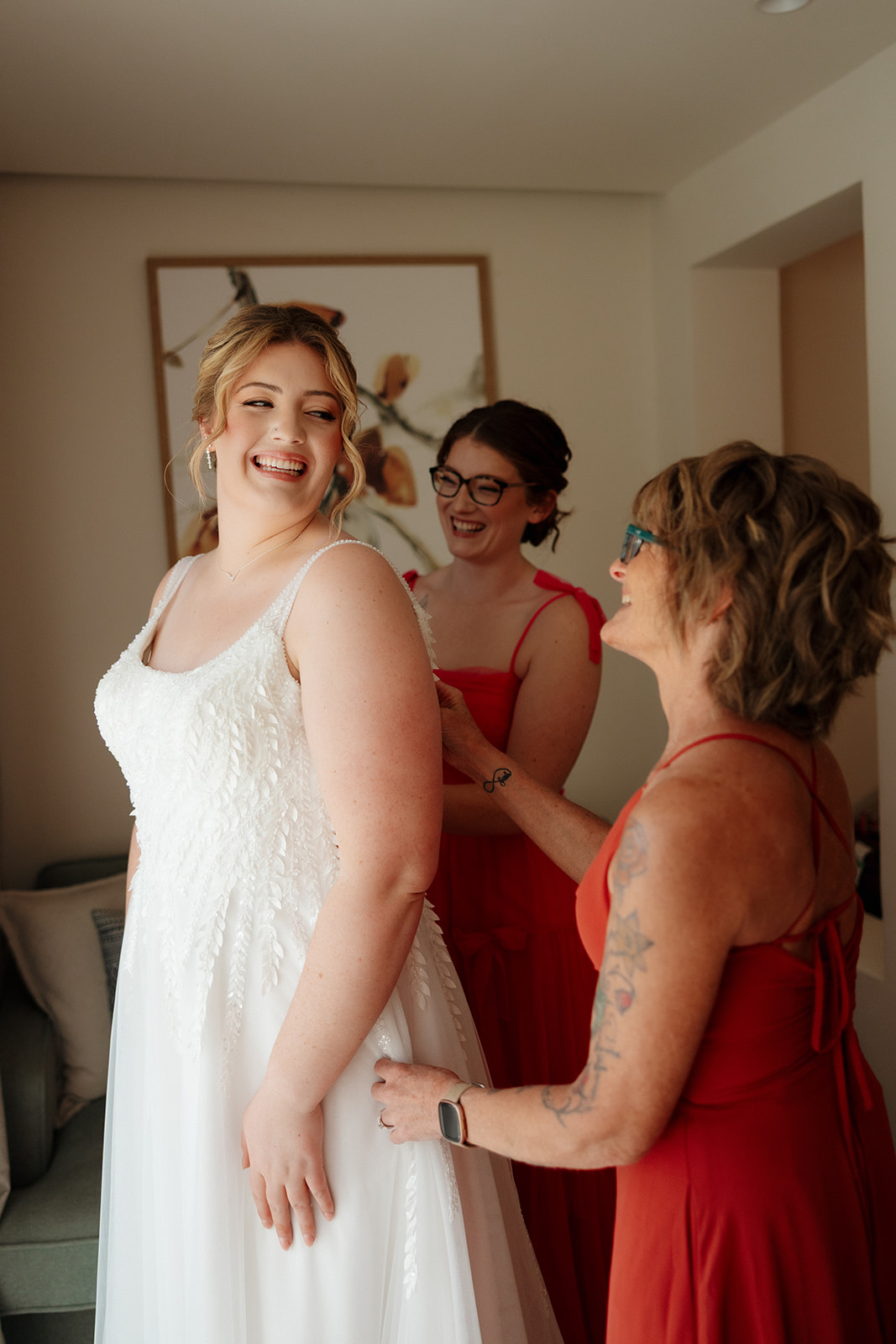 Bride smiling while getting into her dress by window light before a wedding in Florida
