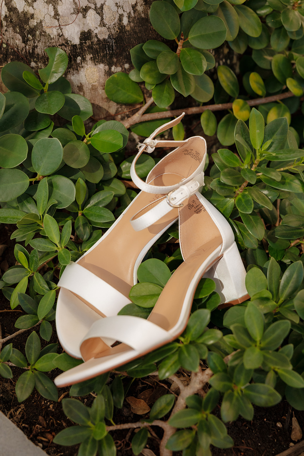 White bridal heels styled in tropical greenery for a beach wedding detail
