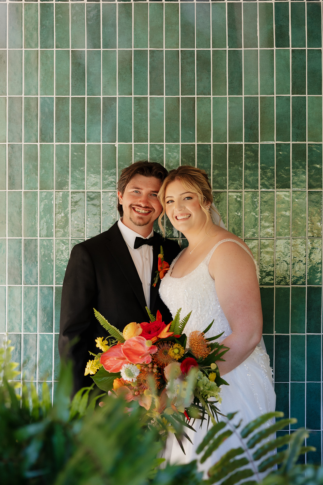 Couple posing with vibrant tropical bouquet against tiled wall during a wedding in Florida