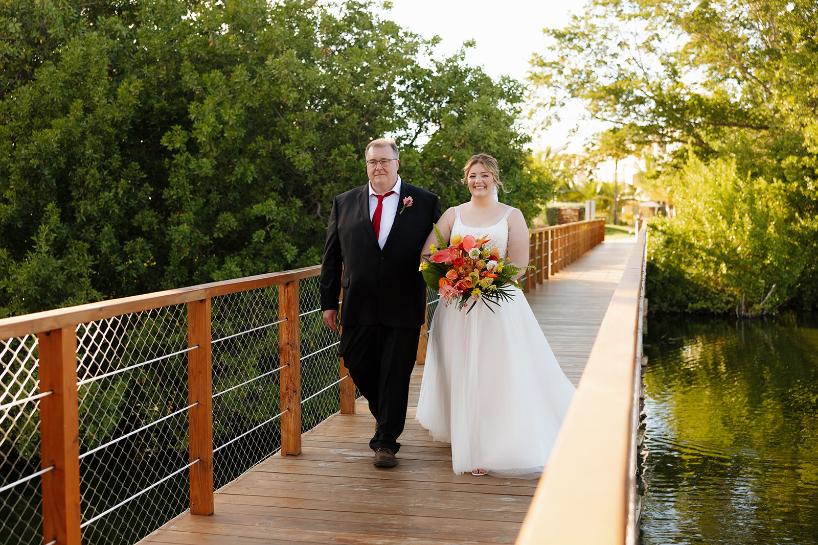 Bride walking with her father across wooden bridge toward ceremony at a wedding in Florida
