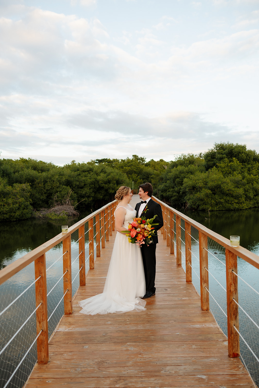 Bride and groom standing together on wooden bridge surrounded by tropical greenery after their wedding
