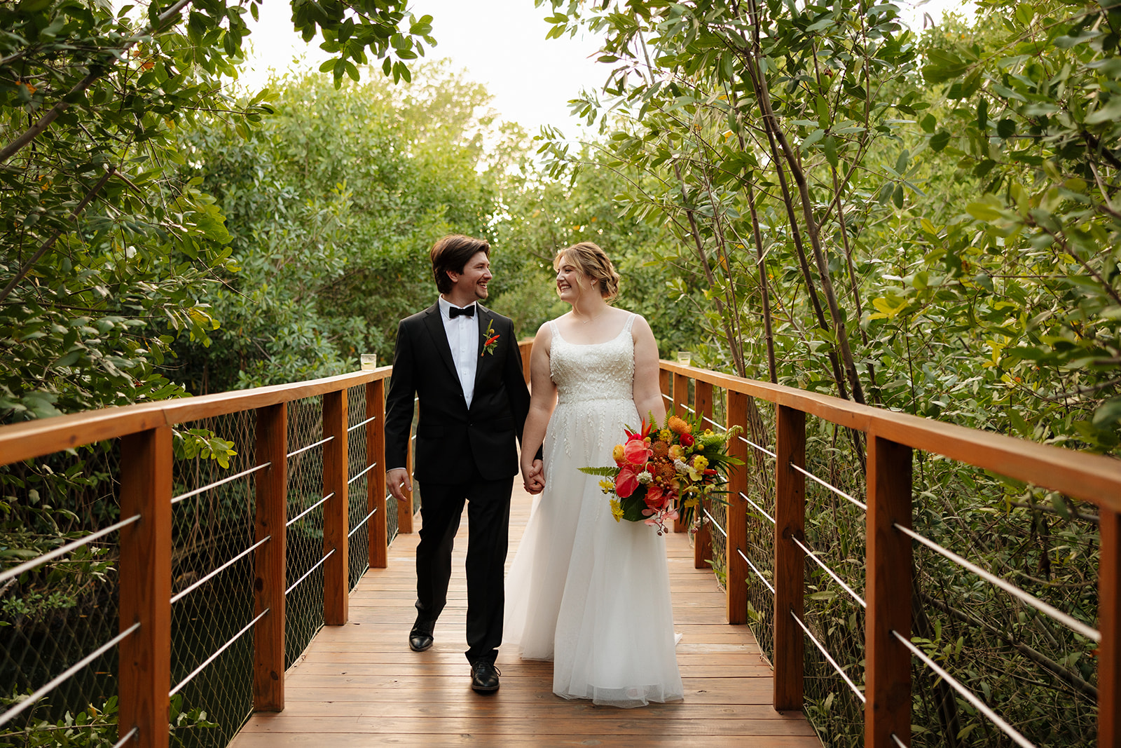 Bride and groom walking hand in hand along wooden path through lush greenery after a wedding in Florida
