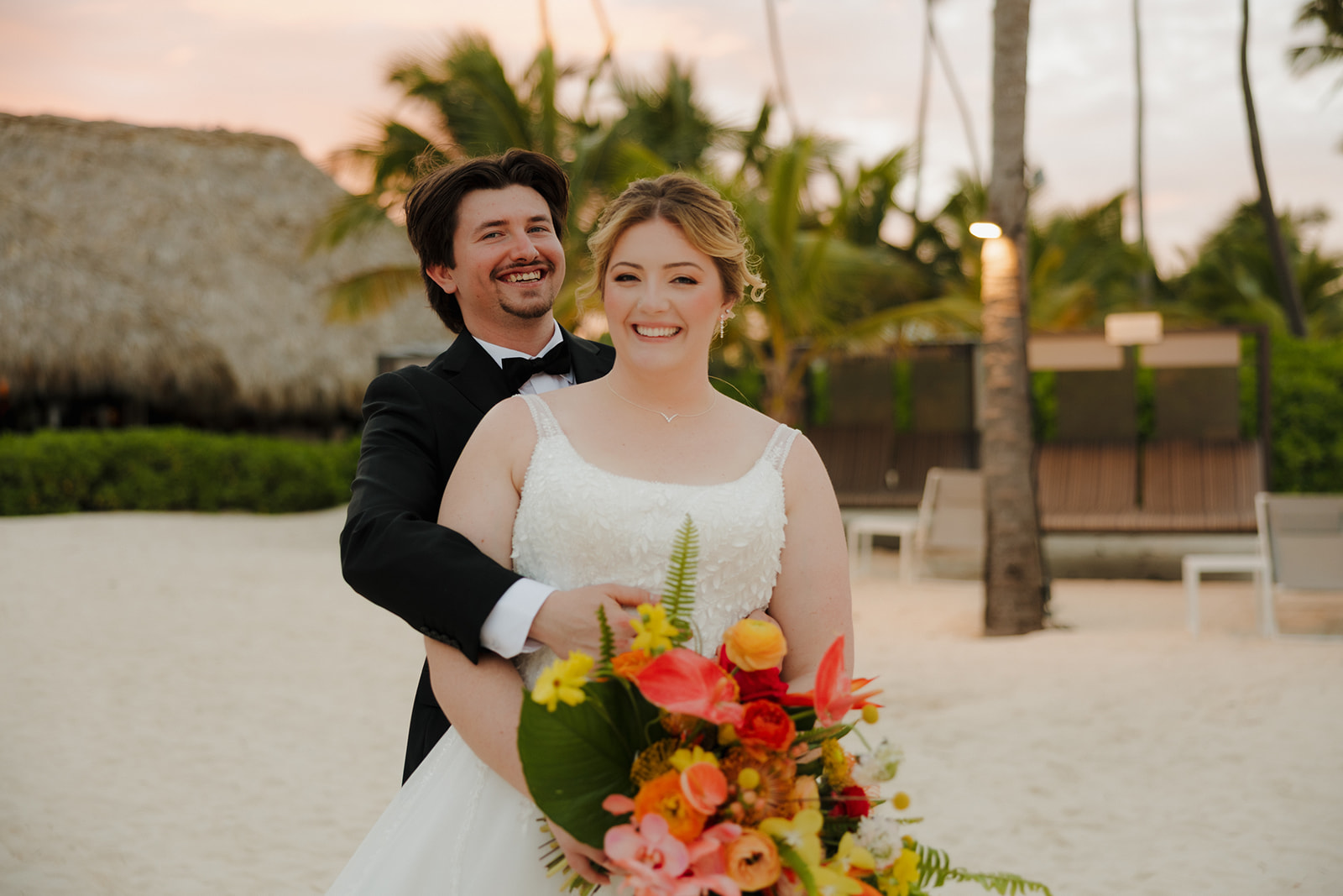 Newlywed couple smiling with tropical bouquet during sunset portraits for a wedding in Florida
